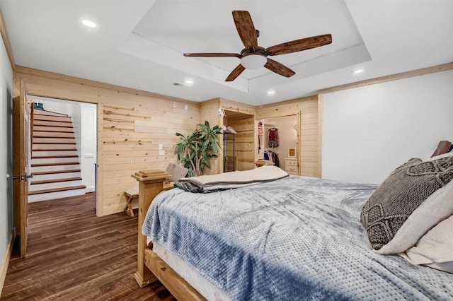 bedroom with ceiling fan, wooden walls, dark hardwood / wood-style floors, a raised ceiling, and a closet