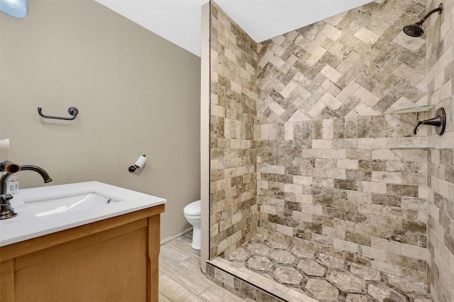 bathroom featuring vanity, tiled shower, hardwood / wood-style floors, and toilet