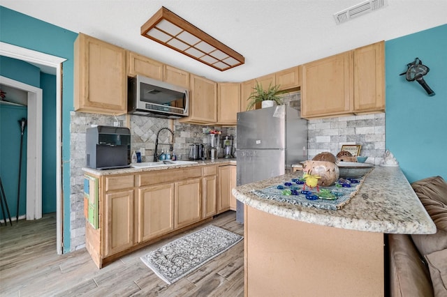 kitchen featuring appliances with stainless steel finishes, light brown cabinetry, sink, backsplash, and light hardwood / wood-style floors