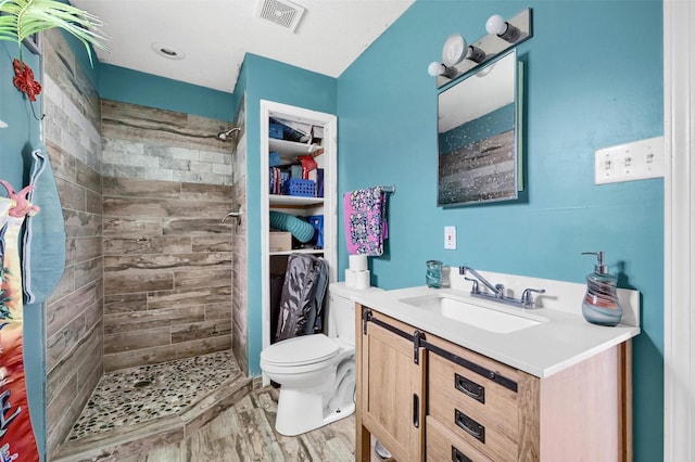 bathroom featuring hardwood / wood-style floors, vanity, a tile shower, and toilet