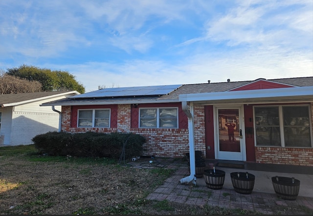 ranch-style house featuring brick siding, solar panels, and roof with shingles
