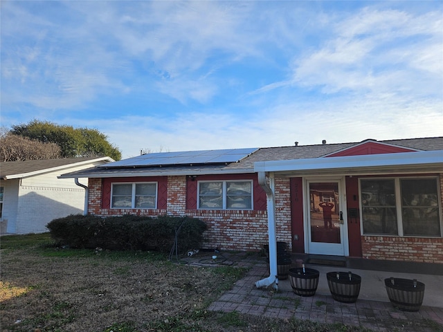 ranch-style home featuring brick siding, roof mounted solar panels, and a shingled roof