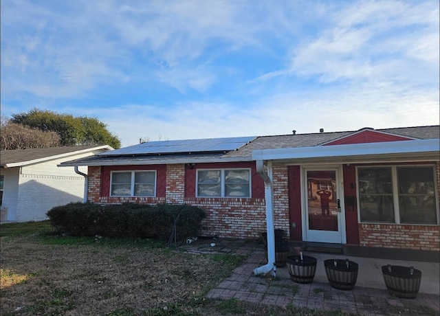 ranch-style home with brick siding, solar panels, and roof with shingles