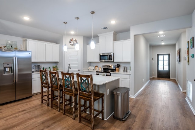 kitchen featuring visible vents, light countertops, wood finished floors, stainless steel appliances, and a kitchen island with sink