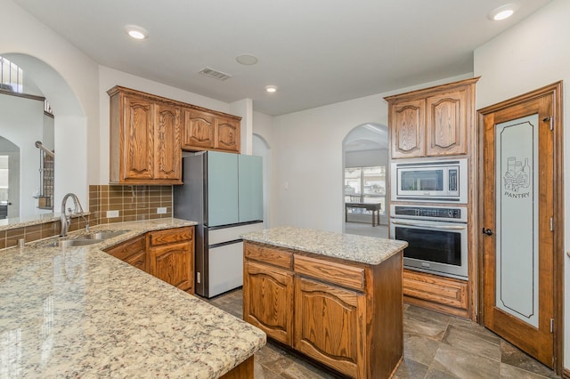 kitchen with sink, light stone counters, a center island, appliances with stainless steel finishes, and decorative backsplash