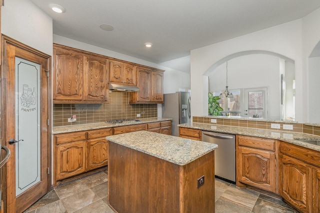 kitchen featuring light stone counters, appliances with stainless steel finishes, a kitchen island, pendant lighting, and backsplash