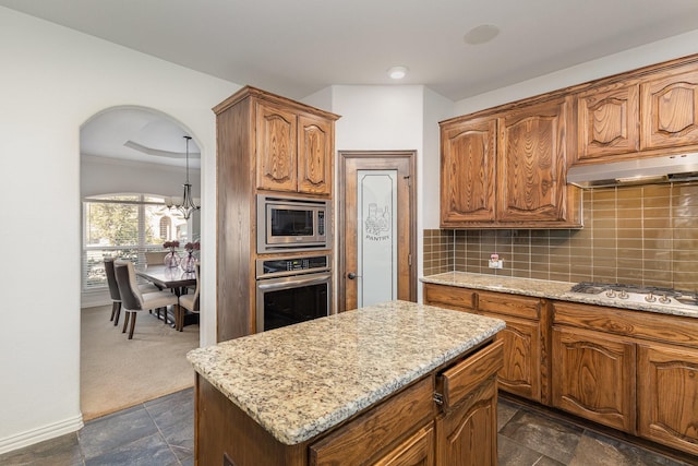 kitchen with decorative backsplash, dark colored carpet, a center island, light stone counters, and stainless steel appliances