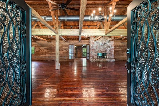 unfurnished living room with beamed ceiling, dark hardwood / wood-style flooring, a stone fireplace, and wooden ceiling