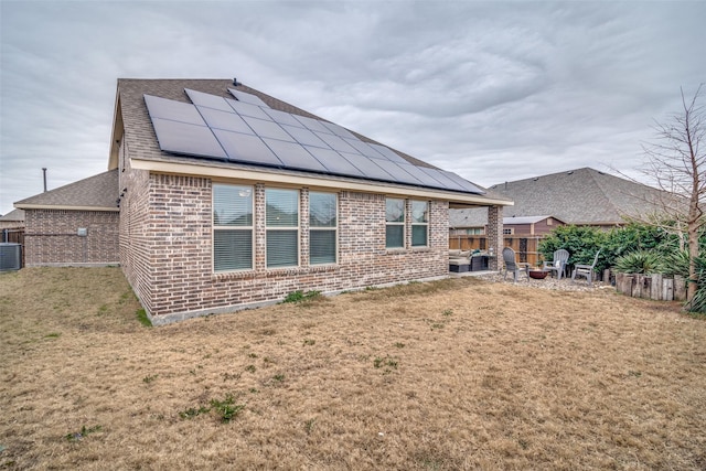 back of property with solar panels, cooling unit, a lawn, and a fire pit