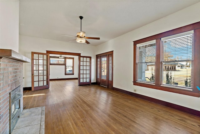 unfurnished living room featuring french doors, ceiling fan, wood-type flooring, and a brick fireplace