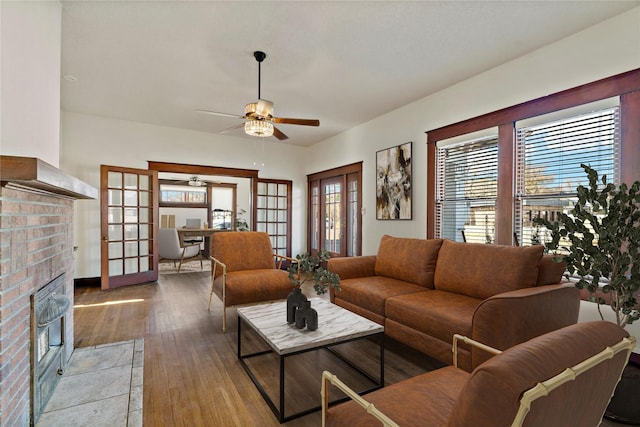 living room featuring wood-type flooring, a brick fireplace, ceiling fan, and french doors