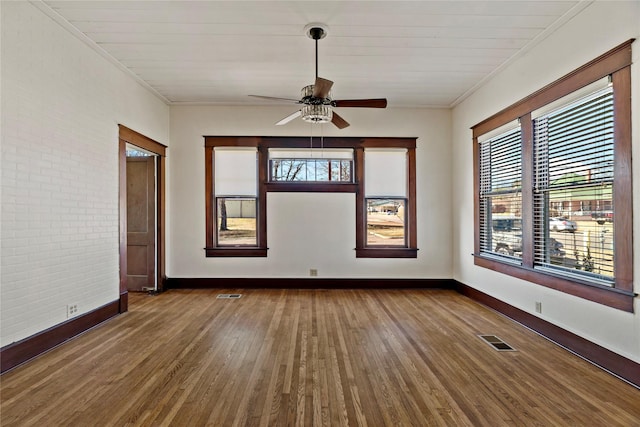 unfurnished room featuring hardwood / wood-style flooring, ornamental molding, brick wall, and ceiling fan