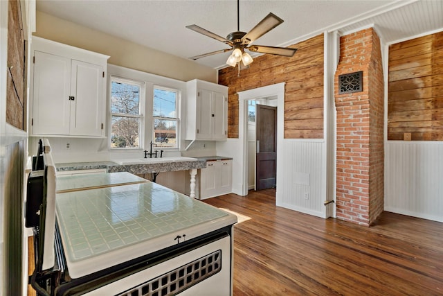 kitchen with sink, white cabinetry, wood-type flooring, wooden walls, and ceiling fan