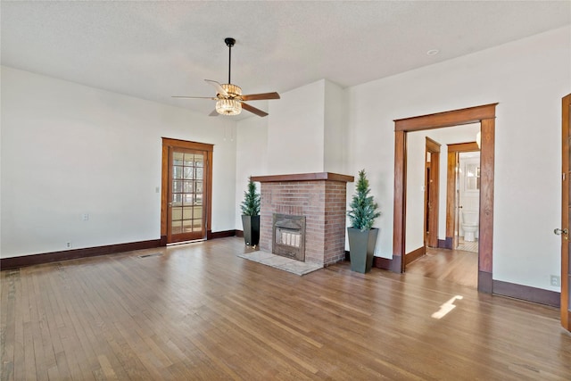 unfurnished living room featuring a brick fireplace, wood-type flooring, a textured ceiling, and ceiling fan