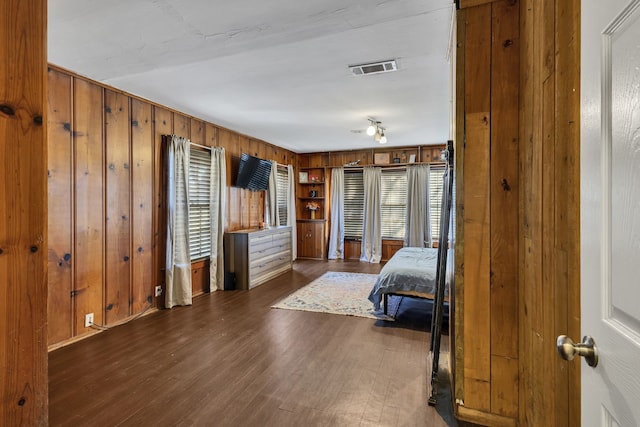 bedroom with multiple windows, wooden walls, and dark hardwood / wood-style floors