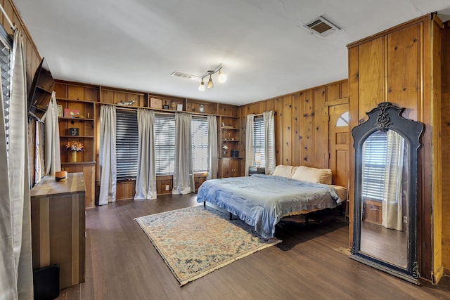 bedroom with multiple windows, dark hardwood / wood-style flooring, and wood walls