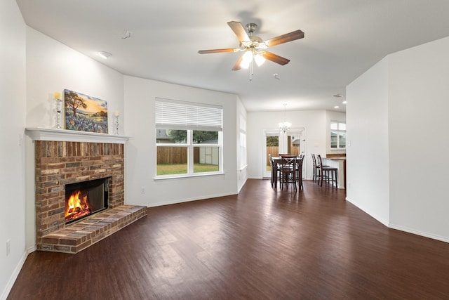 unfurnished living room featuring a brick fireplace, ceiling fan with notable chandelier, a wealth of natural light, and dark hardwood / wood-style floors