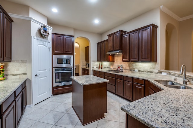 kitchen featuring sink, appliances with stainless steel finishes, a center island, tasteful backsplash, and light stone counters