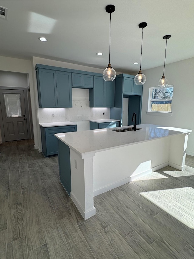 kitchen with sink, tasteful backsplash, decorative light fixtures, an island with sink, and hardwood / wood-style flooring