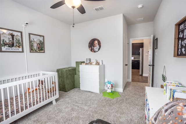 bedroom with ceiling fan, stainless steel fridge, light colored carpet, and a crib