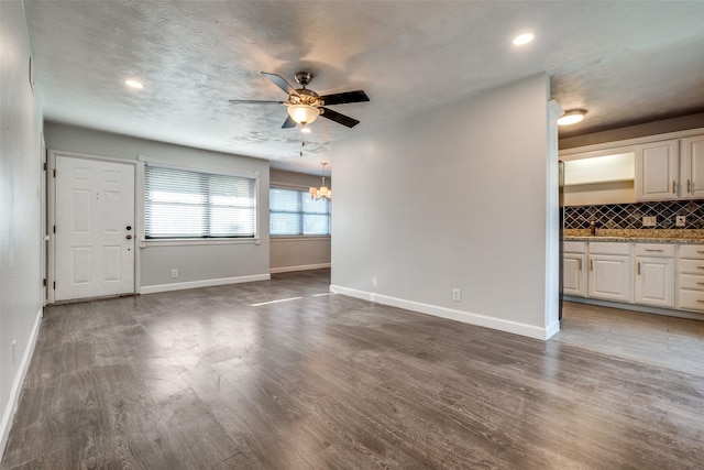 unfurnished living room with ceiling fan with notable chandelier, dark wood-type flooring, and a textured ceiling