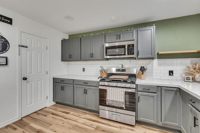 kitchen with backsplash, stainless steel appliances, light hardwood / wood-style floors, and gray cabinetry