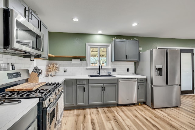 kitchen featuring sink, appliances with stainless steel finishes, gray cabinetry, decorative backsplash, and light wood-type flooring