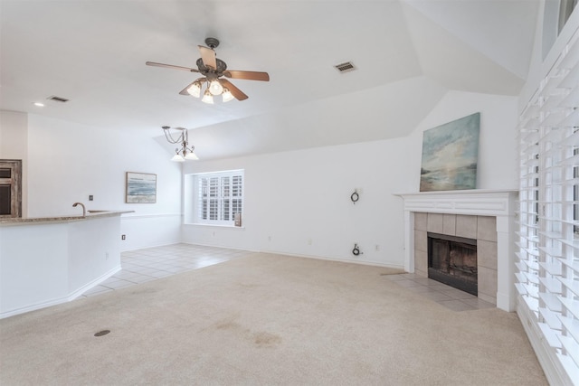 unfurnished living room featuring a tile fireplace, vaulted ceiling, light carpet, and ceiling fan