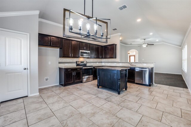 kitchen featuring lofted ceiling, pendant lighting, stainless steel appliances, light stone counters, and a kitchen island