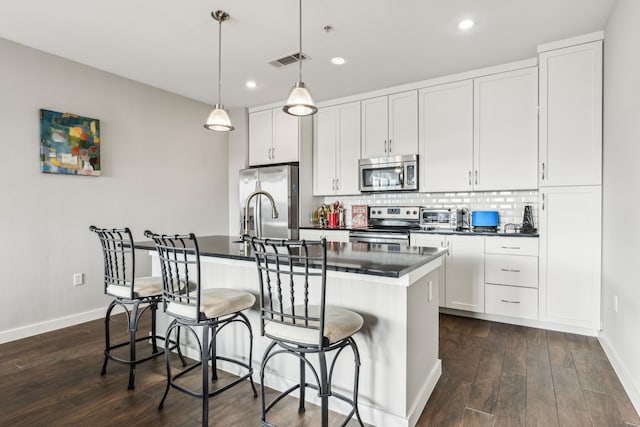 kitchen with appliances with stainless steel finishes, hanging light fixtures, a kitchen breakfast bar, white cabinets, and a center island with sink