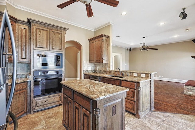 kitchen with sink, ceiling fan, appliances with stainless steel finishes, a center island, and tasteful backsplash