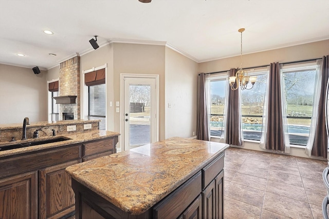 kitchen with sink, hanging light fixtures, ornamental molding, light stone countertops, and a kitchen island