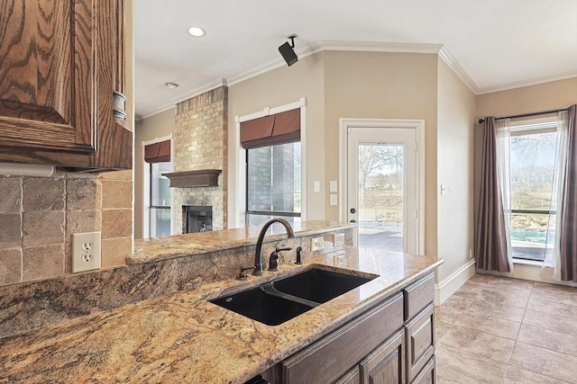 kitchen with ornamental molding, light stone countertops, sink, and a fireplace