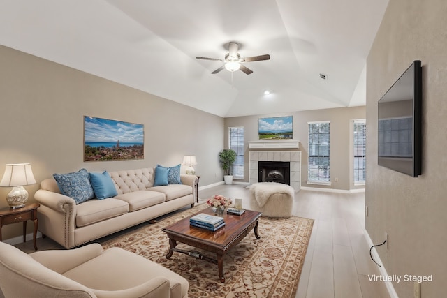 living room with lofted ceiling, a tiled fireplace, light hardwood / wood-style flooring, and ceiling fan