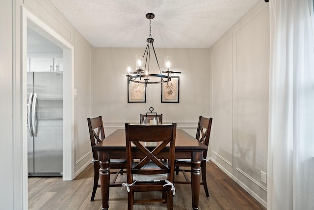 dining area featuring a notable chandelier, wood-type flooring, and a textured ceiling