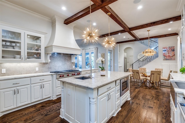 kitchen featuring sink, custom exhaust hood, appliances with stainless steel finishes, a kitchen island with sink, and white cabinets