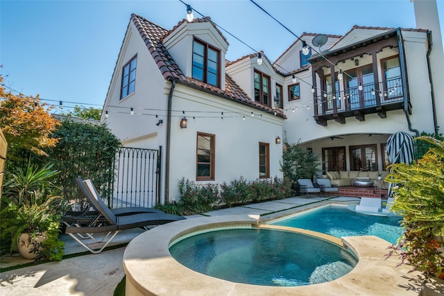 rear view of property with an outdoor living space, an in ground hot tub, a balcony, and a patio area