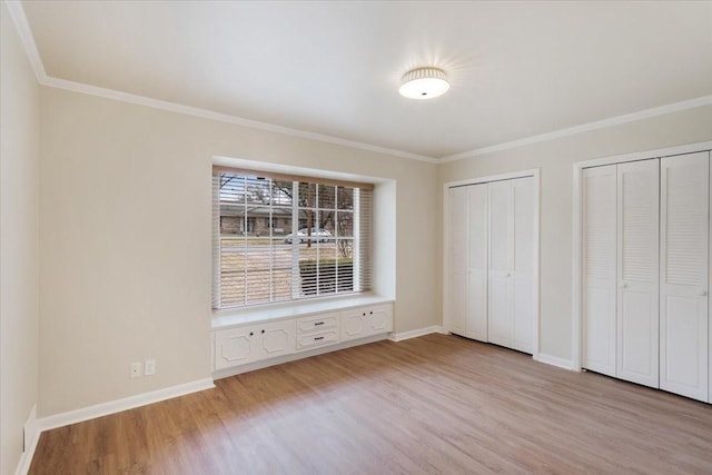 unfurnished bedroom with ornamental molding, light wood-type flooring, and two closets