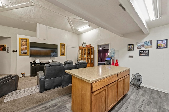 kitchen with wood-type flooring, a center island, vaulted ceiling with beams, and a textured ceiling