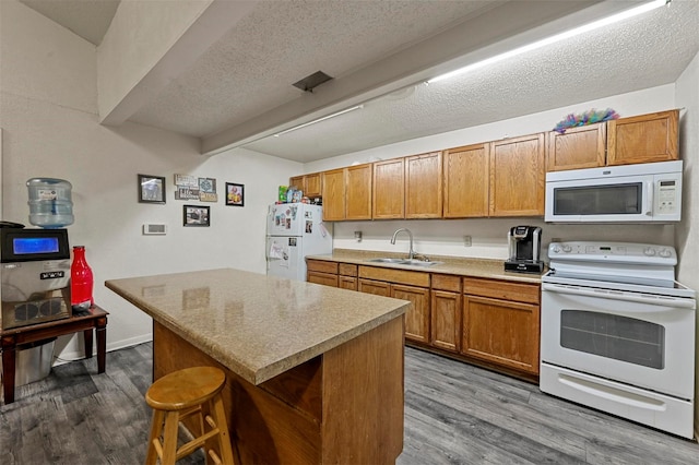 kitchen featuring sink, white appliances, hardwood / wood-style floors, a kitchen breakfast bar, and a kitchen island