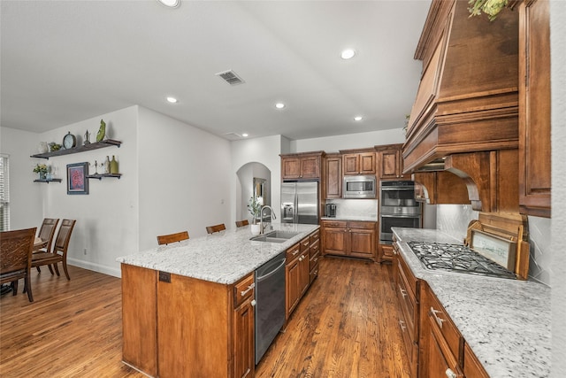 kitchen with sink, a breakfast bar, built in appliances, light stone counters, and a center island with sink