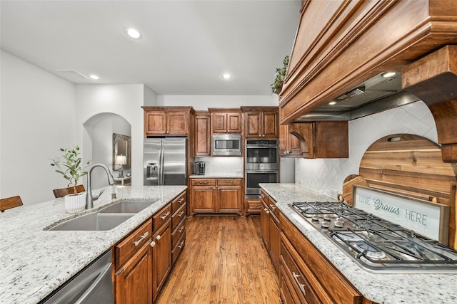 kitchen with sink, backsplash, light stone counters, stainless steel appliances, and light hardwood / wood-style flooring