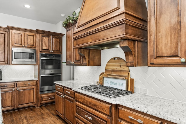 kitchen with light stone counters, backsplash, dark wood-type flooring, and appliances with stainless steel finishes