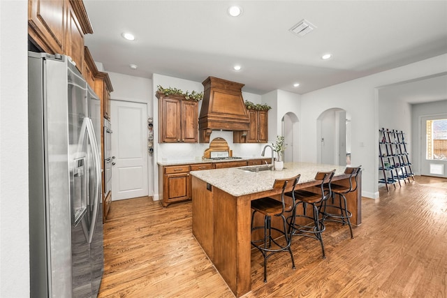 kitchen featuring premium range hood, a breakfast bar area, light stone counters, a center island with sink, and stainless steel appliances