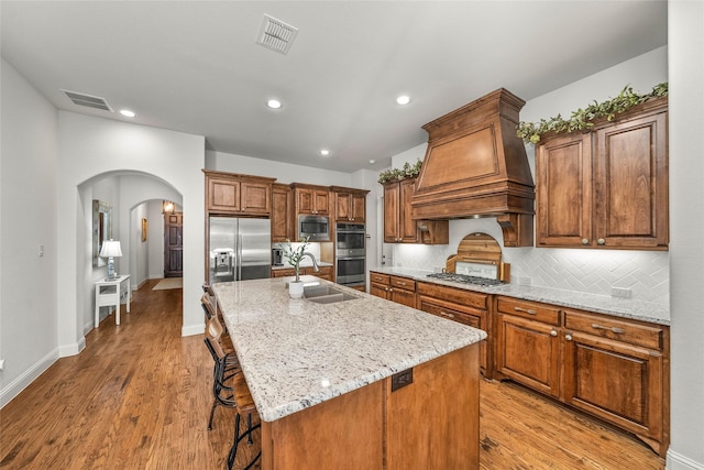 kitchen featuring premium range hood, a kitchen bar, sink, built in appliances, and an island with sink