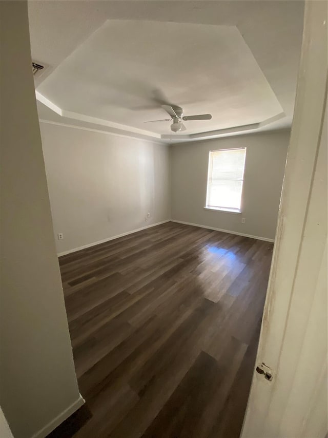 empty room featuring dark hardwood / wood-style floors, ceiling fan, and a tray ceiling