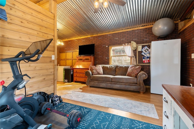 exercise room featuring wooden walls, ceiling fan, and brick wall