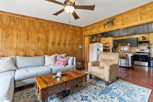 living room with ceiling fan, dark hardwood / wood-style flooring, and wood walls