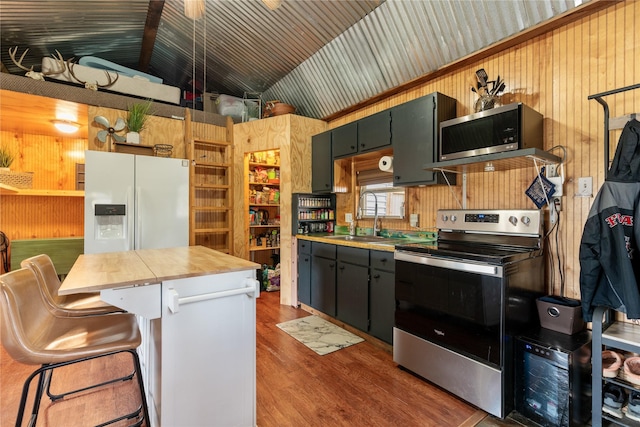 kitchen featuring wood walls, lofted ceiling, sink, a kitchen bar, and stainless steel appliances