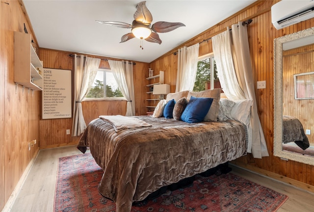 bedroom featuring ceiling fan, light hardwood / wood-style floors, a wall unit AC, and wood walls